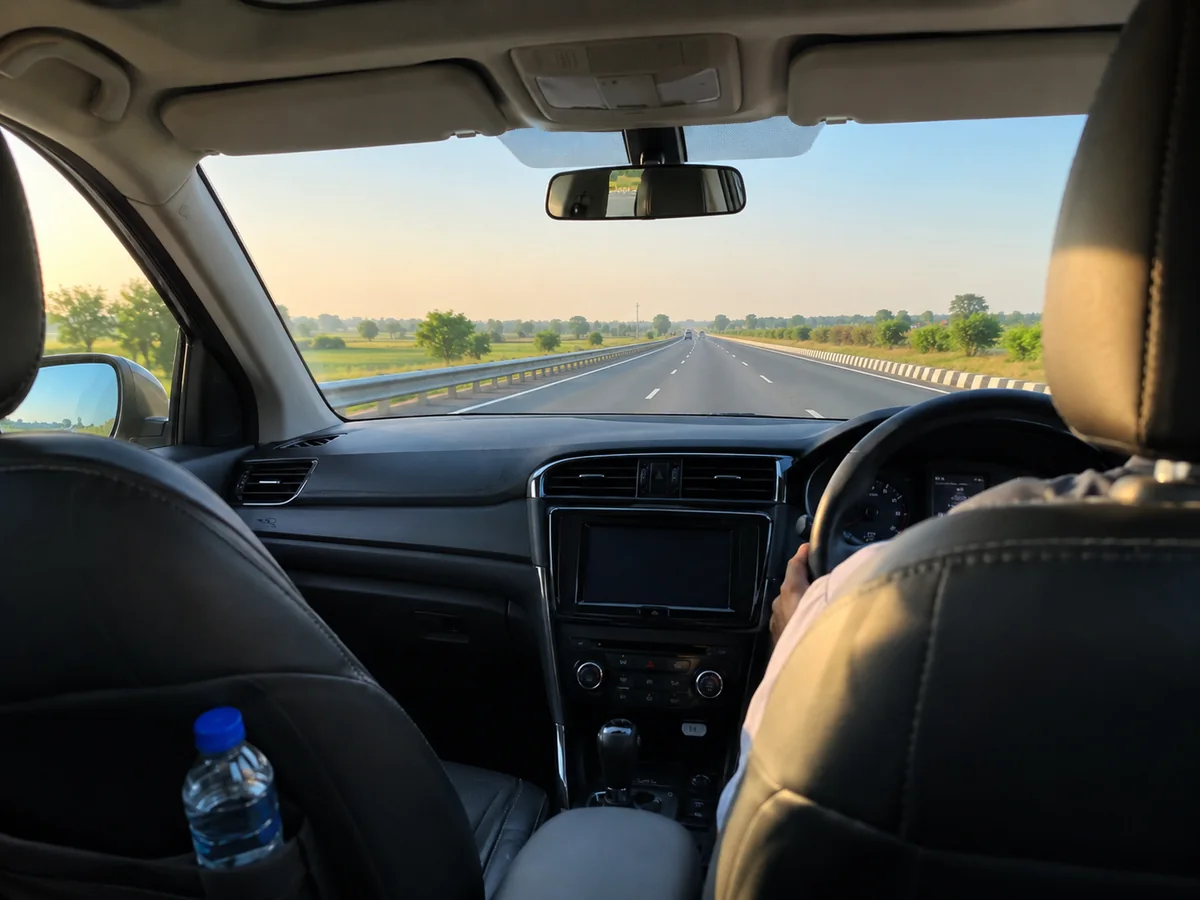 View from the back seat of a private car on a wide Indian expressway through green fields