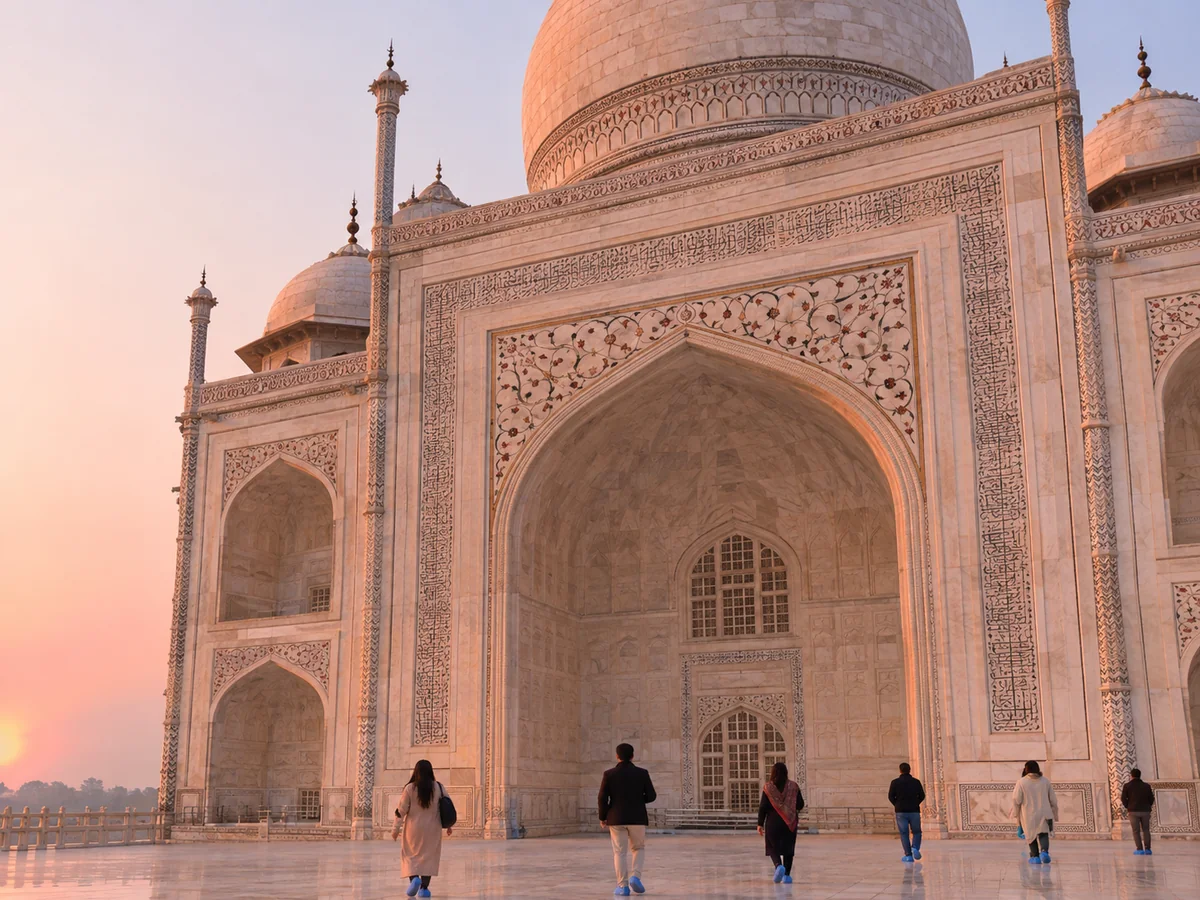 The Taj Mahal mausoleum in soft pink sunrise light with visitors on the marble platform